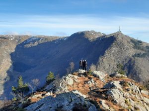 Studerende på bjergtop i Norge med panoramaudsigt over fjelde, klipper og dramatisk norsk natur i solskin.