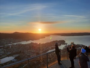 Solnedgang over Bergen i Norge med udsigt til fjord, havn, bjerge og panoramaudsigt over byen.